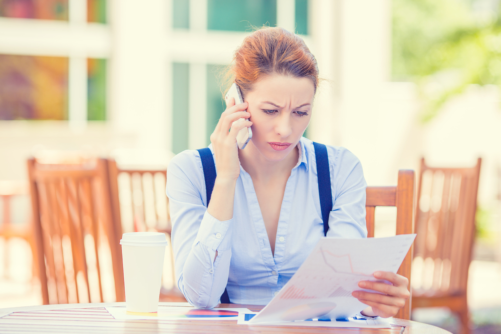 An unhappy person speaks on the phone while holding a financial document.