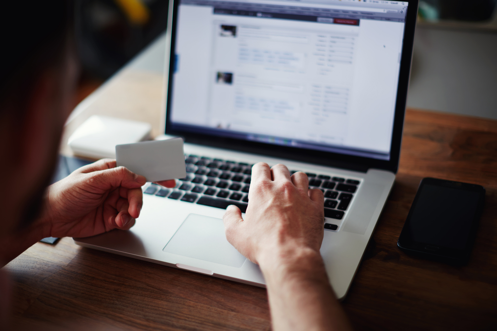 A person typing on their laptop with one hand while holding a credit card in the other.