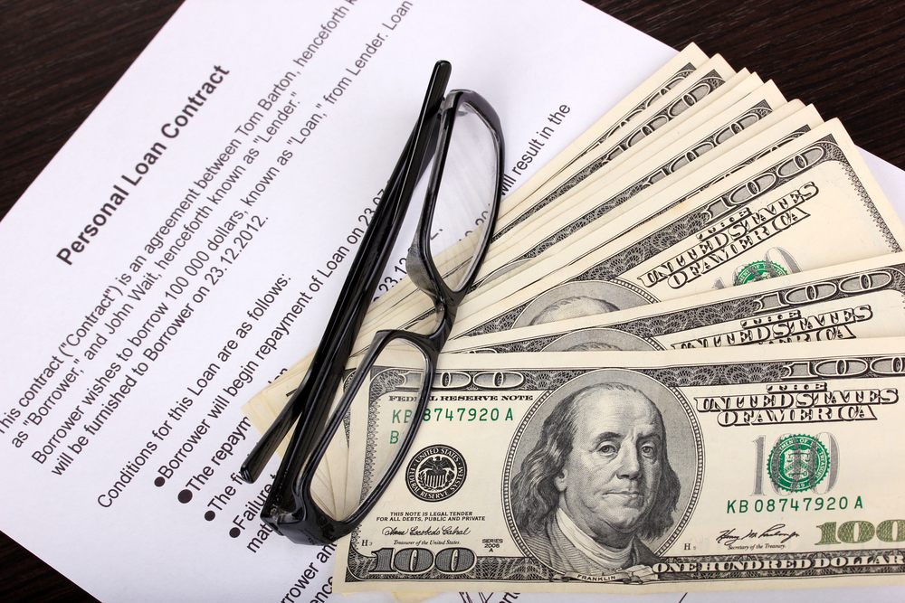Eyeglasses and $100 bills sit on top of a personal loan contract.