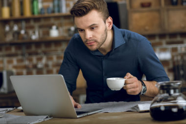 A person holding a coffee cup while working on their laptop.
