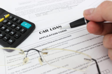 Eyeglasses and a calculator sit on top of a car loan application form.