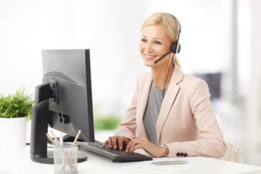 A credit repair representative wears a headset and sits at their computer while helping a person.