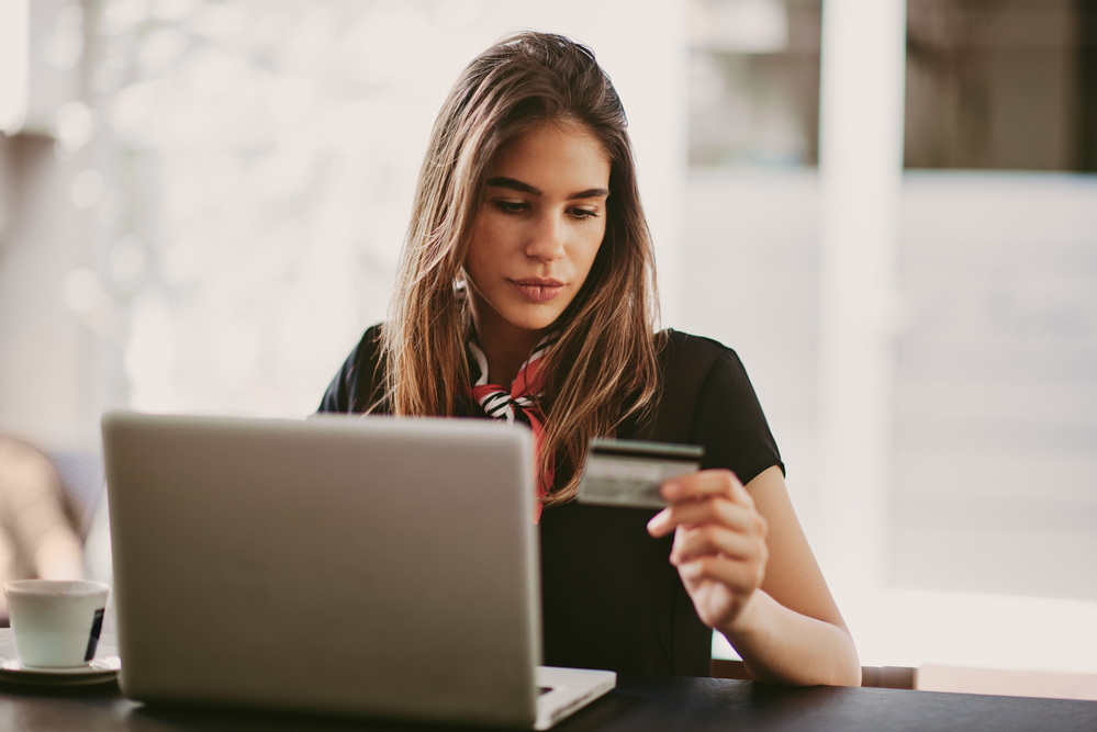 A person using their laptop at their desk, reading numbers off of a credit card.