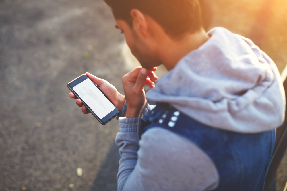 A person standing outdoors, using their phone.