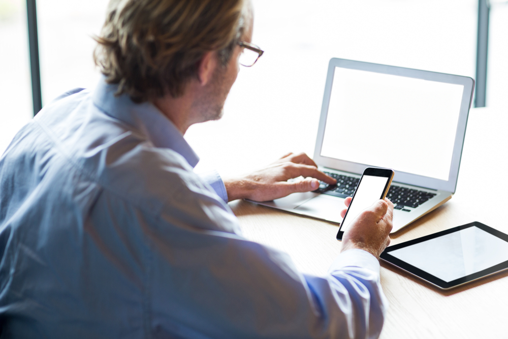 A person working on their computer while holding their phone.