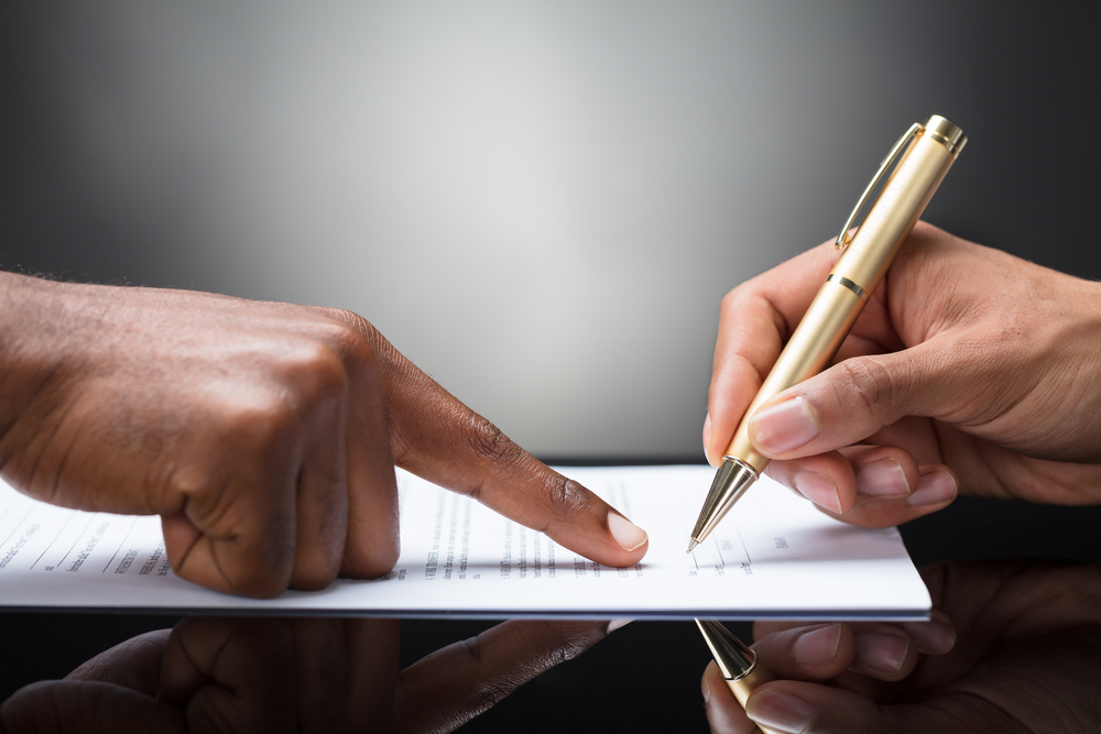 A mortgage lender points to a contract as a person signs it.