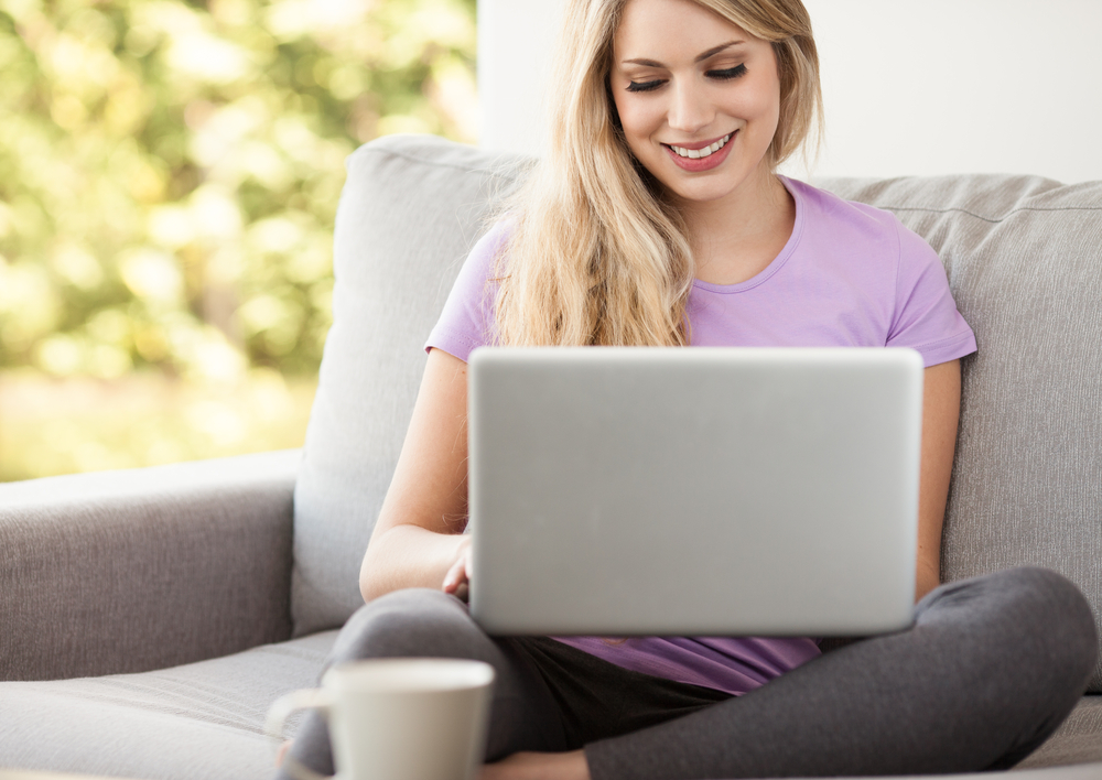 A person sitting on their couch, smiling as they work on their laptop.