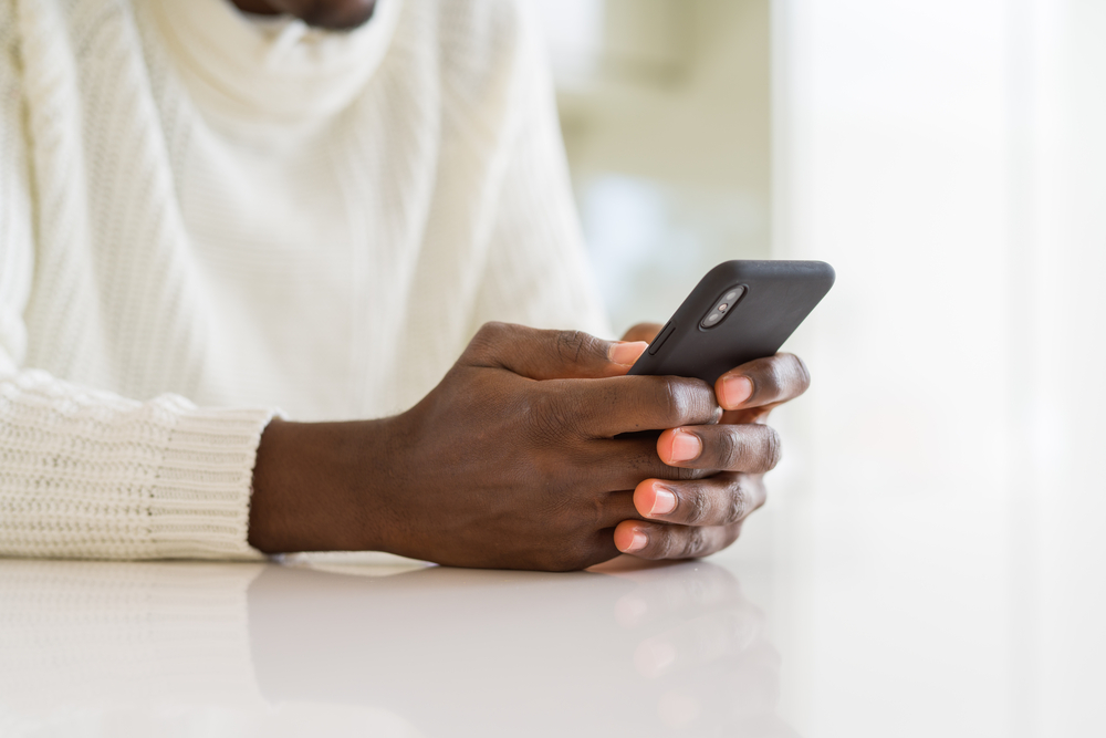 A person in a white sweater, sitting down to use their phone.