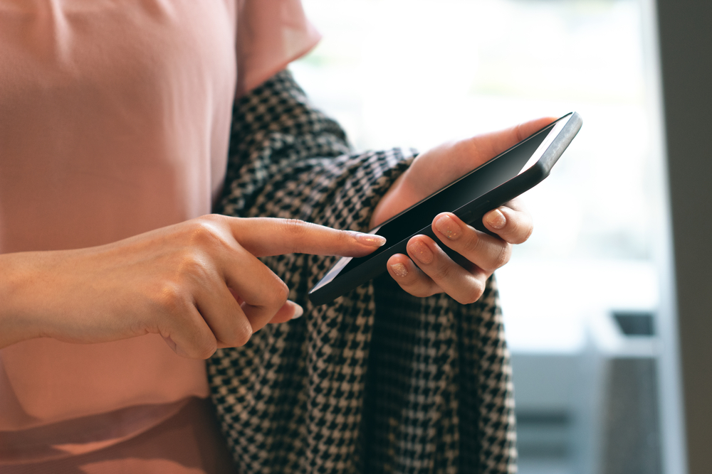 A closeup of a person checking their phone with a checkered shirt draped over their arm.