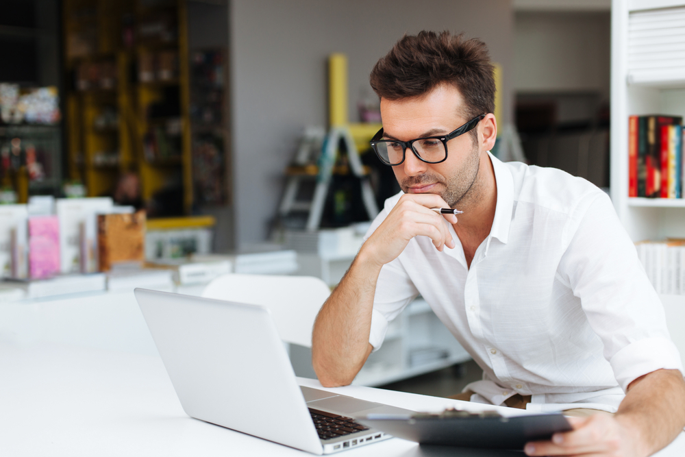 A person holds their hand to their chin as they are working on their laptop.