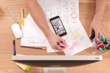 View of desk from above with computer and phone with man drawing charts