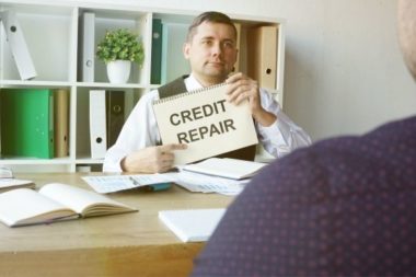 Man at desk showing sign that says "credit repair" to a client across desk