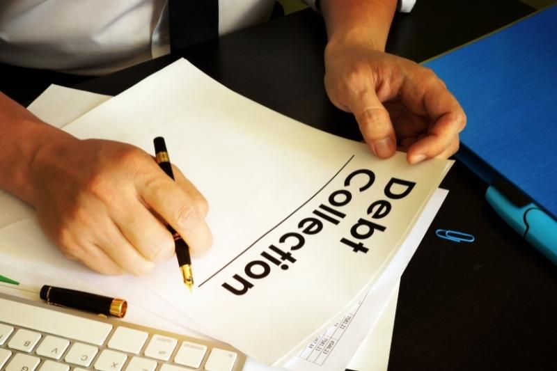 Man's hands holding pen to paper on desk labeled Debt Collections like what may be received from Account Services