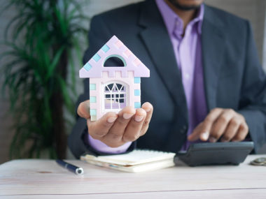 man in purple suit jacket holding a toy house in his hand